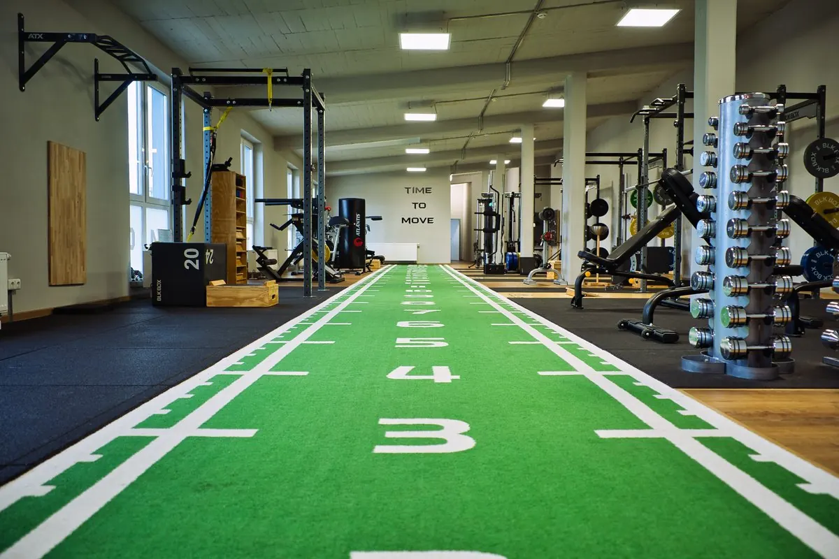 Räume eines Trainingsstudios mit grüner Sprintbahn, Racks und Hanteln