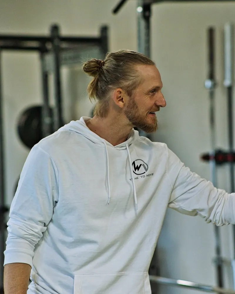 Lachender Trainer im weißen Hoodie im Trainingsstudio