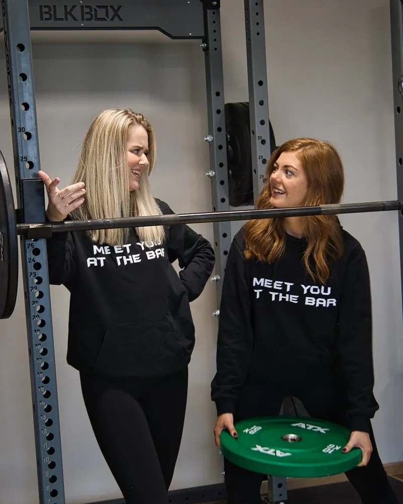 Zwei Mitarbeiterinnen im Gespräch an einer Langhantel im Trainingsstudio